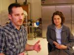A young man and woman in a baking facility, sitting on stools, talking