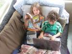 one child reads while another looks at a computer screen