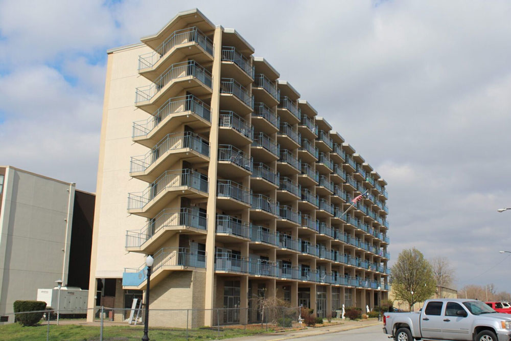The photo shows a tall, tan apartment complex.