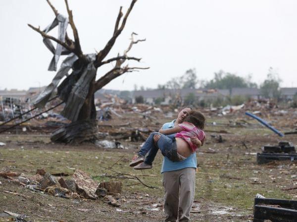 A woman carries her child through a field near the collapsed Plaza Towers Elementary School in Moore, Okla., on Monday A tornado as much as a mile wide with winds up to 200 mph roared through the Oklahoma City suburbs flattening entire neighborhoods, setting buildings on fire and landing a direct blow on an elementary school.