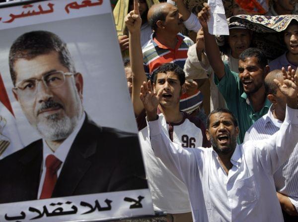 Supporters of Egypt's ousted President Mohammed Morsi shout slogans under his poster following Friday prayers in Nahda square, where protesters installed their camp near Cairo University in Giza, southwest of Cairo, Egypt, Friday, Aug. 9, 2013. Protesters demand Morsi's reinstatement, restoration of the suspended constitution drafted under Morsi and the return of his Islamist-dominated legislative council which was also disbanded. The Arabic on the poster reads,