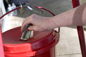 A Corner Market grocery store customer places a dollar in the iconic Salvation Army collection bucket in Jackson, Miss., Wednesday, Nov. 25, 2020, as a bell ringer, unseen, wishes customers a 
