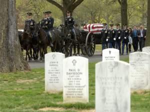 A horse-drawn caisson carries a casket and leads family members through Arlington National Cemetery.