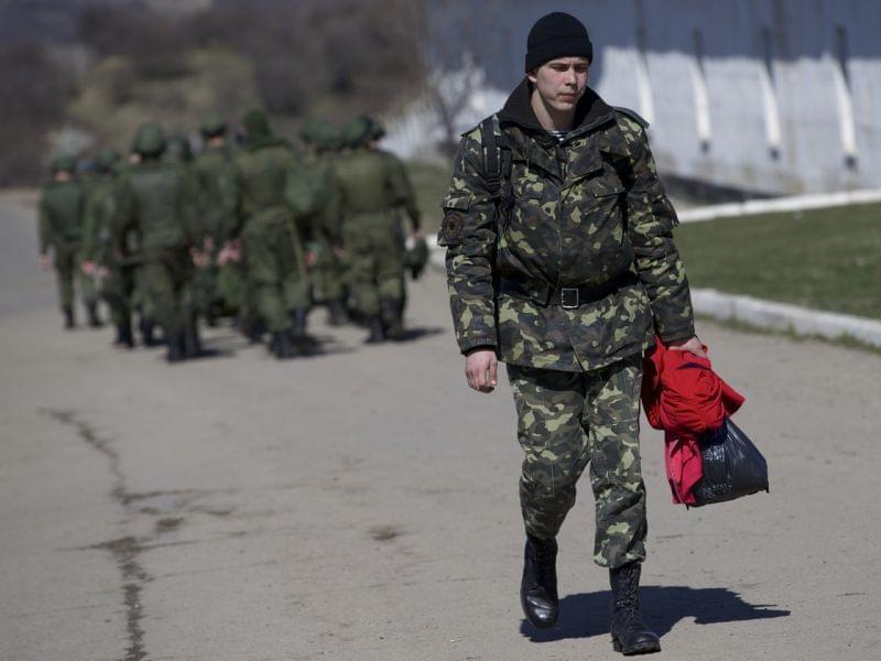 As Russian soldiers walked one way in the distance, a departing Ukrainian soldier carried some of his belongings Friday at a military base in Perevalne, Crimea.