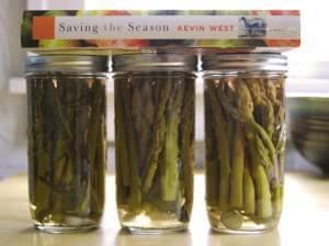 Three jars of pickled asparagus with a cookbook