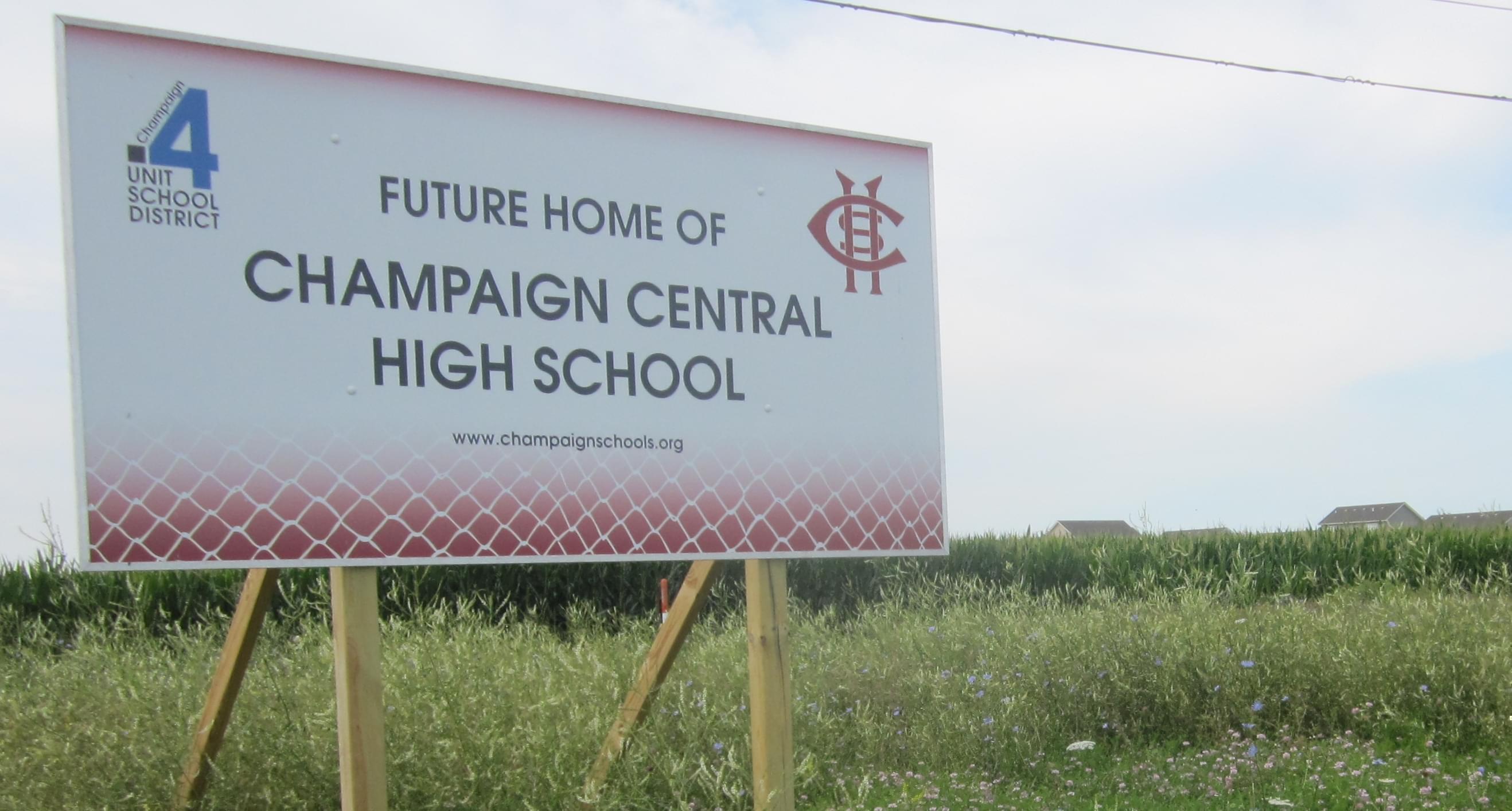 A sign announcing the site of a future Champaign Central High School stands in a field along Olympian Drive on the north edge of Champaign, with the Ashland Park residential subdivision visible in the distance.