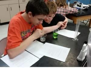 Students stirring a fluid in a beaker in their science class.