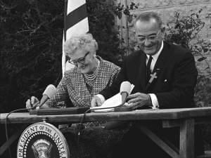 President Lyndon B. Johnson signs the ESEA in 1965 with Kate Deadrich Loney, his first schoolteacher. 