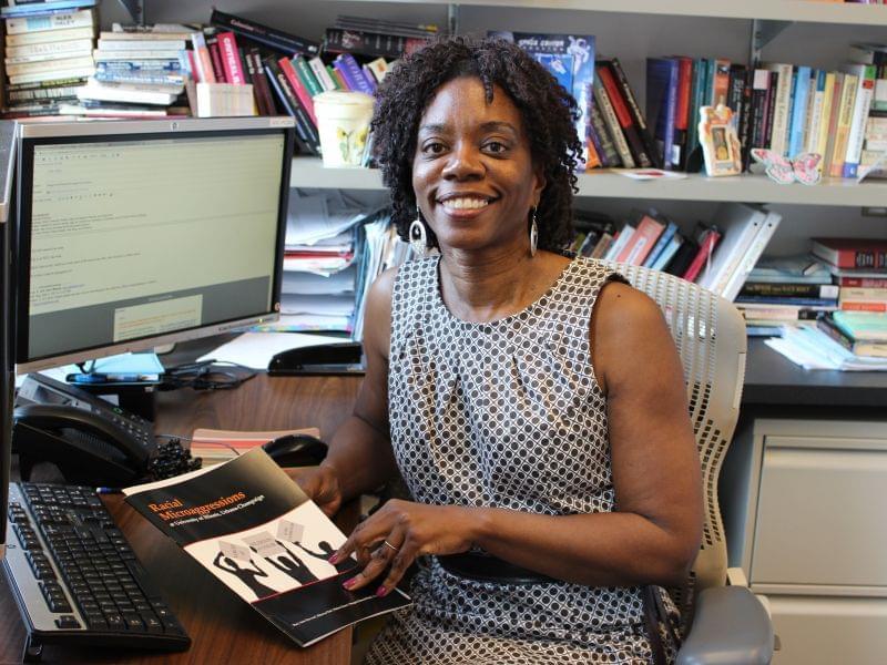 Researcher Ruby Mendenhall sits in her office holding a copy of the Racial Microaggressions in the Classroom report.