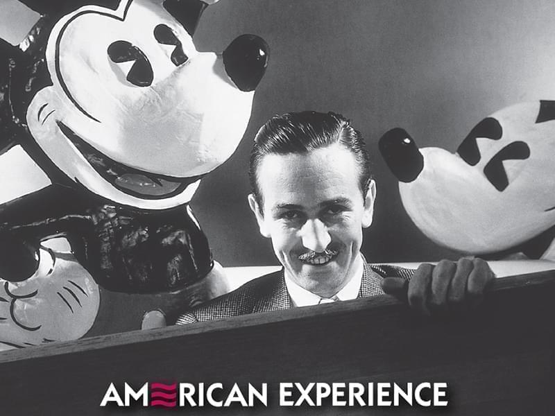 photo of Walt Disney with large Mickey Mouse figures behind him.