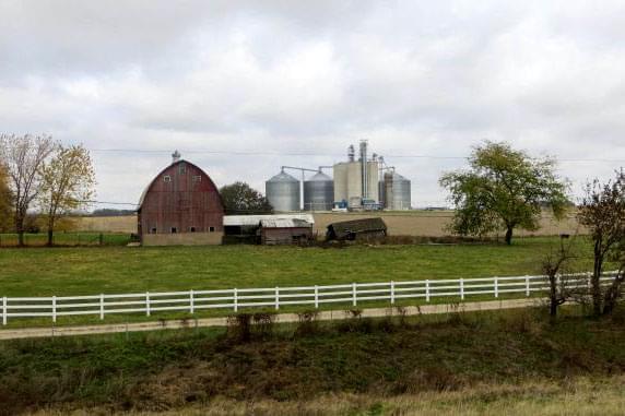 A barn, grain silos, pasture and crop land in a rural area.