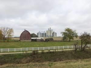 A barn, grain silos, pasture and crop land in a rural area.
