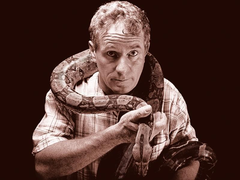 Joel Sartore holds a boa constrictor around his neck