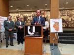 State Senator Andy Manar speaks at the podium at Urbana High School alongside Urbana School District Superintendent. Don Owen and State Senator Scott Bennett. 