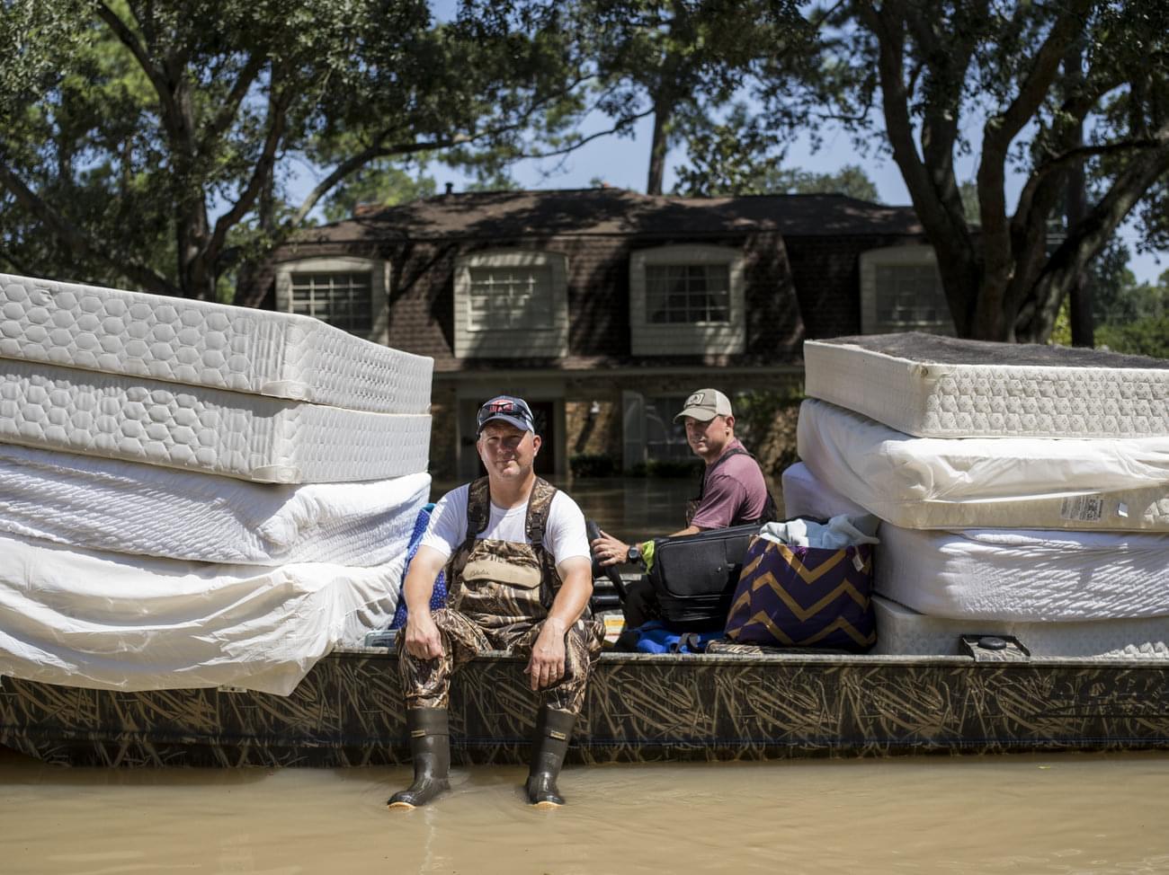 Scott McKnight (left) rides in a boat with his mattresses in the Nottingham Forrest subdivision of Houston on Thursday. Bret Hinkie, a Houston-area commercial airline pilot and a high school friend of McKnight, is volunteering to drive residents to t