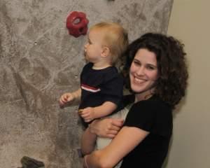 Mom holding  toddler son up next to rock climbing wall