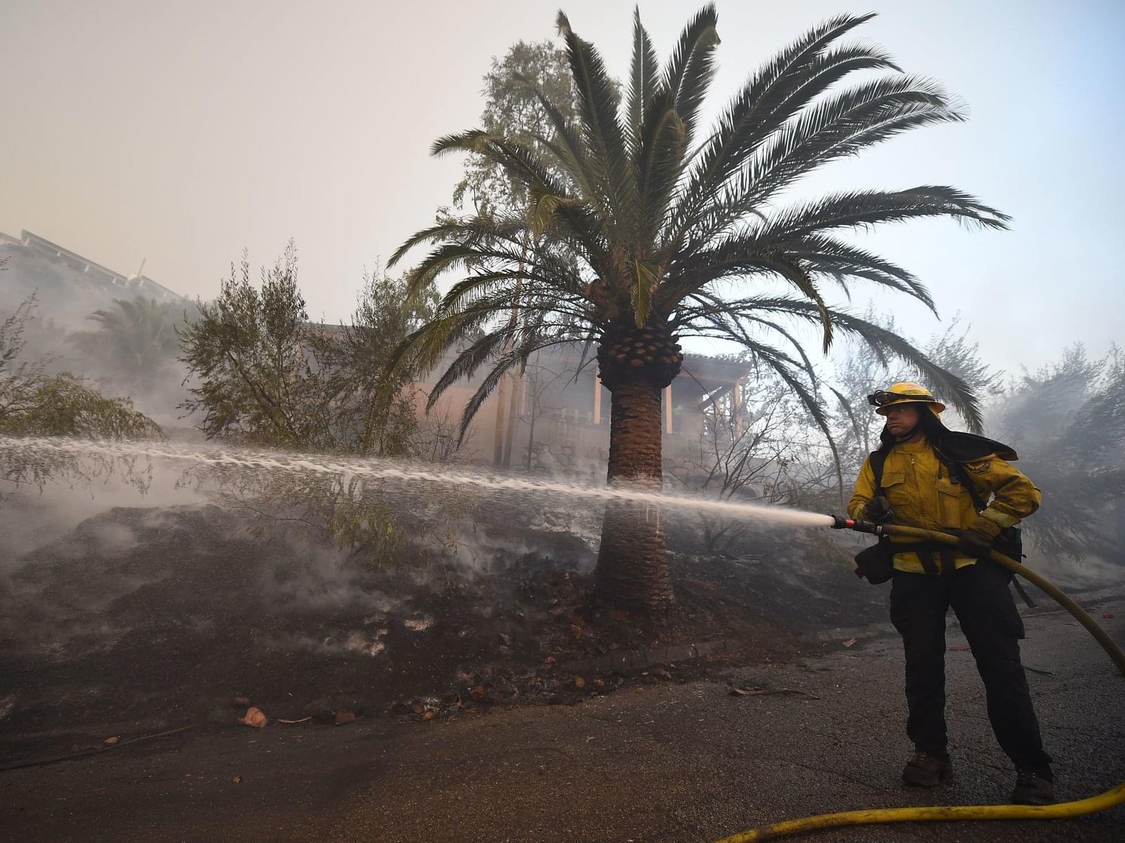 A firefighter douses flames around a house that was saved while the property around it burned as winds picked up and pushed the fire west Saturday in Montecito, Calif.