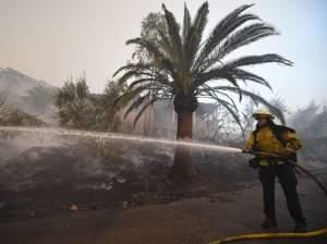 A firefighter douses flames around a house that was saved while the property around it burned as winds picked up and pushed the fire west Saturday in Montecito, Calif. 
