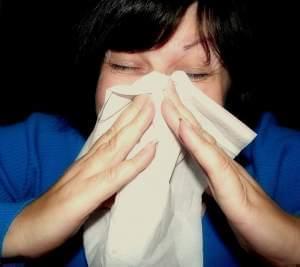 A woman sneezing into a hankerchief. 