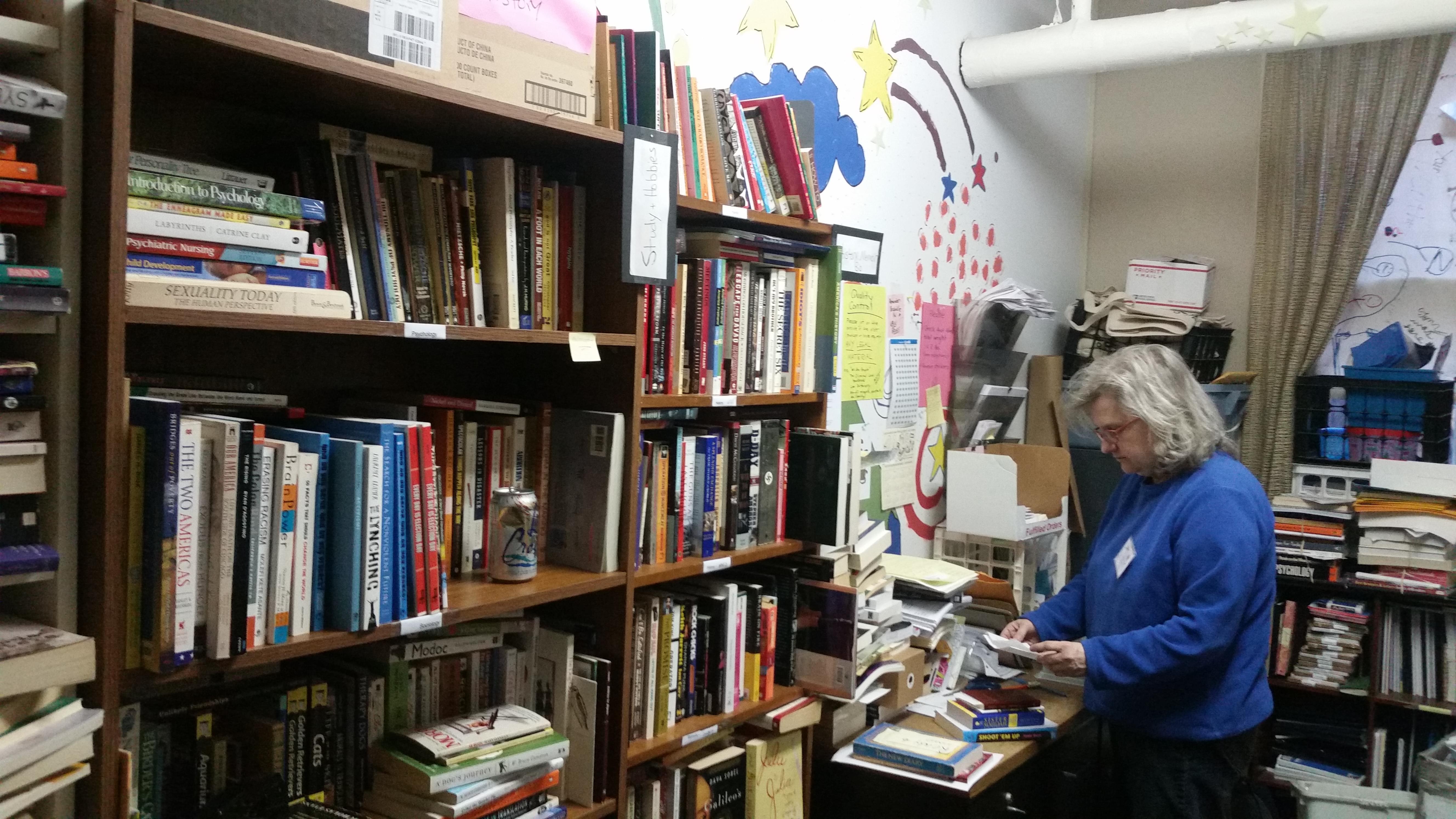 Vicki White, president of Chicago Books to Women in Prison, reads a letter sent from an incarcerated woman. She is standing in a room lined with bookcases and book shelves full of books. 
