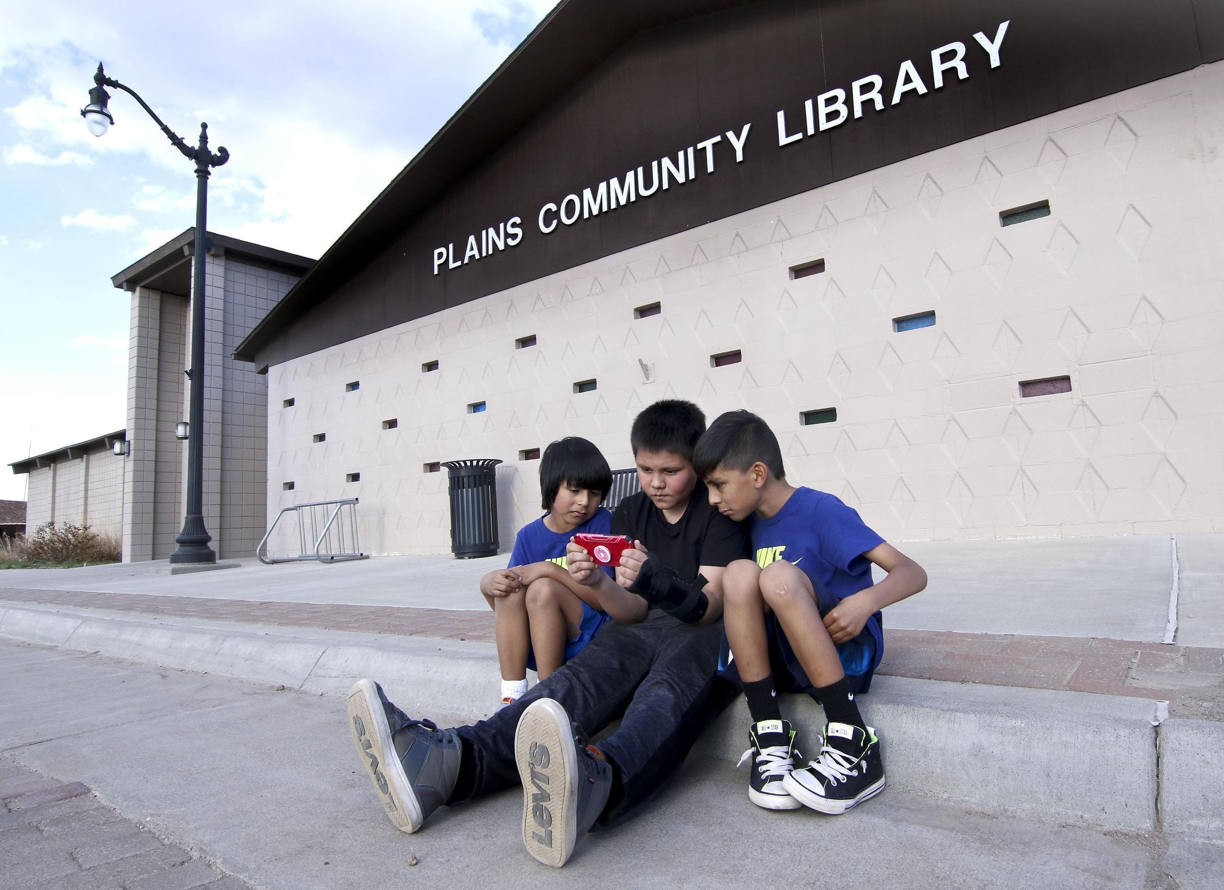 Angel Alvarez, center, holds his phone as he and Eduardo and Giovanni Alvarez watch Youtube videos. They're camped outside the library in Plains, Kansas, using the Wi-Fi signal because broadband can be hard to come by in town.