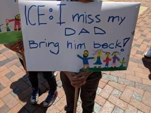 A child holds a sign that says: "ICE: I miss my dad. Bring him back."