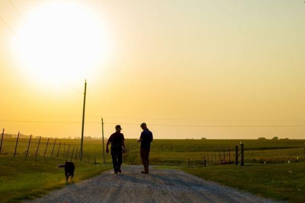 Two men and a dog in a farm driveway.