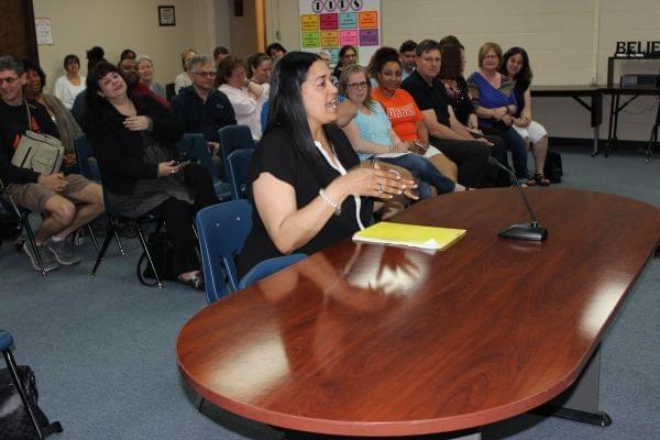 Jennifer Ivory-Tatum behind a desk speaking to the Urbana District 116 School Board with meeting attendees seated behind her.