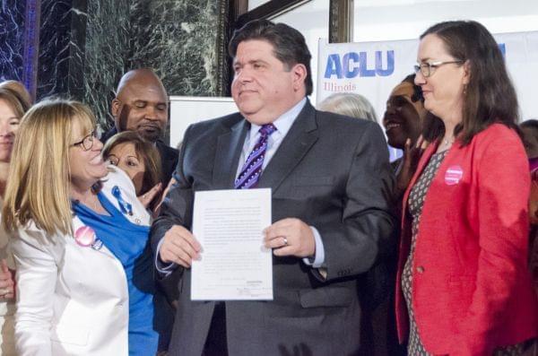 Gov. J.B. Pritzker displays the newly-signed Reproductive Health Act as supporters Melinda Bush and Kelly Cassidy look on.