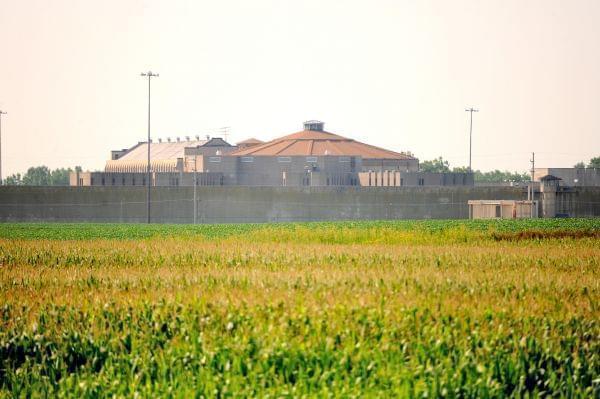 An image of a crop field with a large prison wall behind it. 