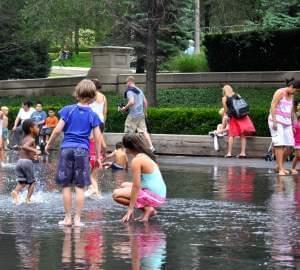 People playing in a fountain during hot weather.