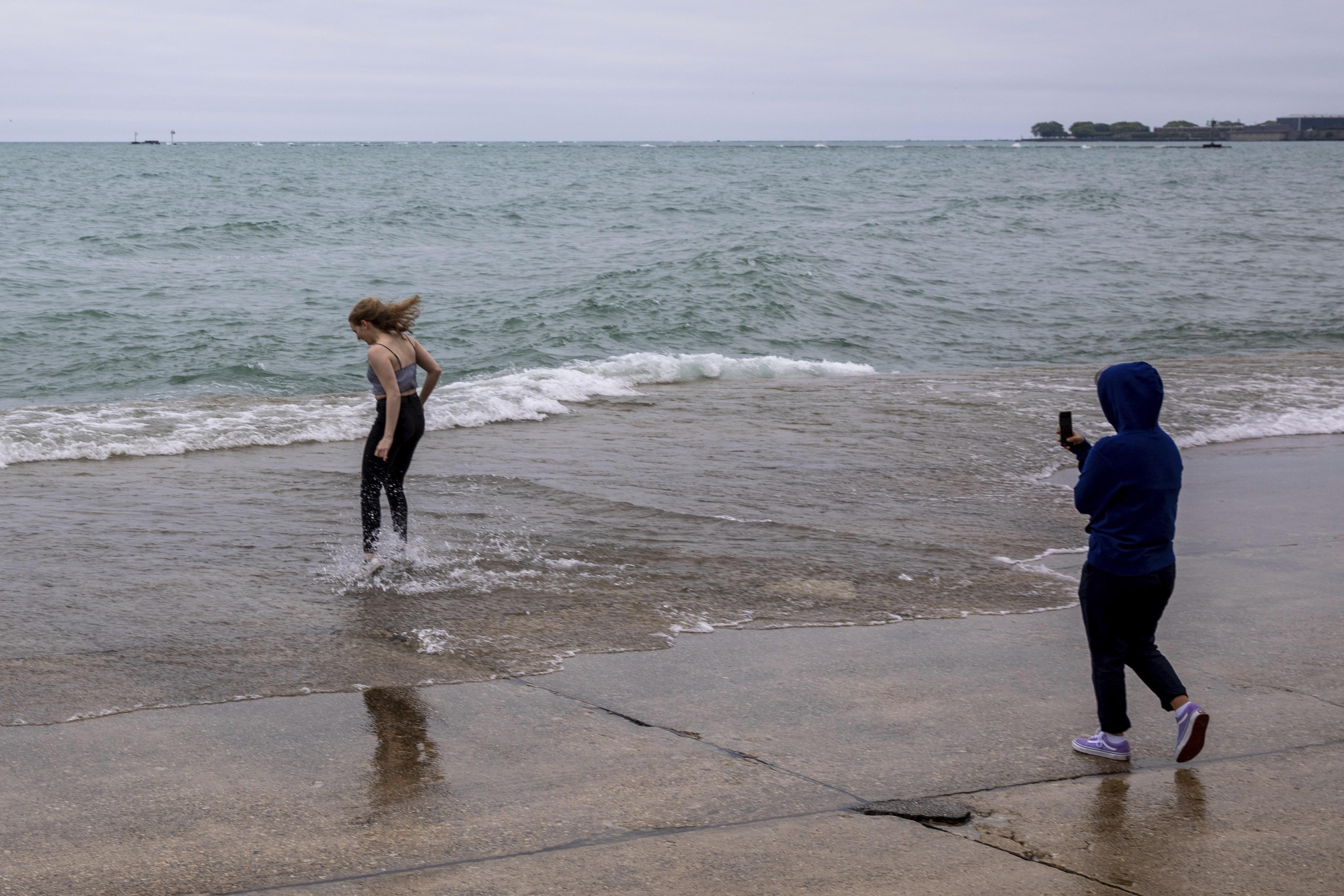 A woman jumps into the shallow water of Lake Michigan as her companion takes her picture at Chicago's Oak Street Beach, Thursday, June 20, 2019.
