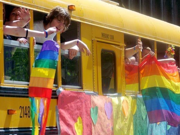 Students leaning out of school bus window with rainbow flags