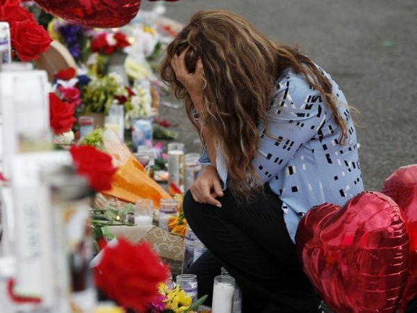 A woman grieves with her head in her hands over a makeshift memorial.