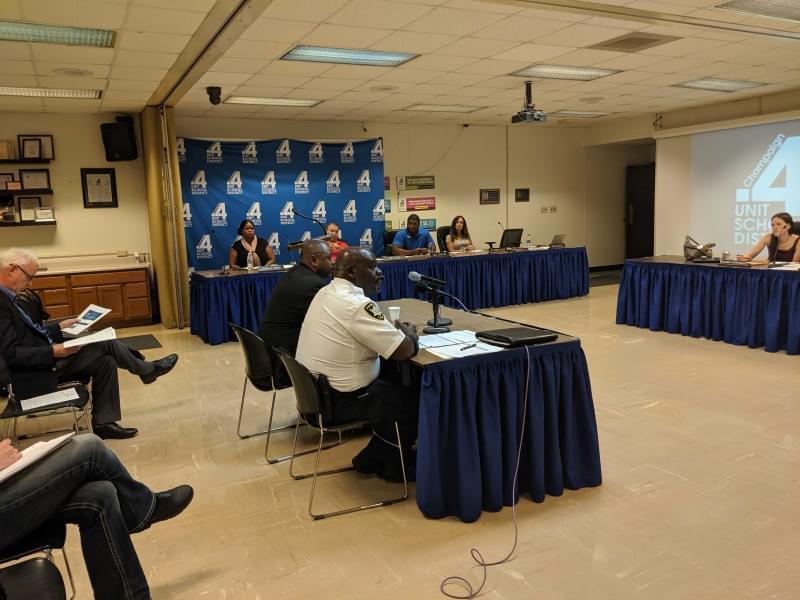 Champaign Police Chief Anthony Cobb and Champaign Unit 4 Director of Achievement and Student Services seated at a table in front of microphones with Unit 4 staff seated around them.