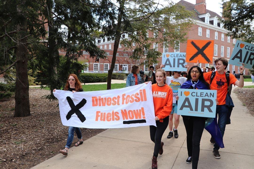 college students holding environmental protest signs march on the campus quad