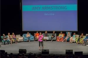 Amy Armstrong speaking on a stage with women listening to her in the background