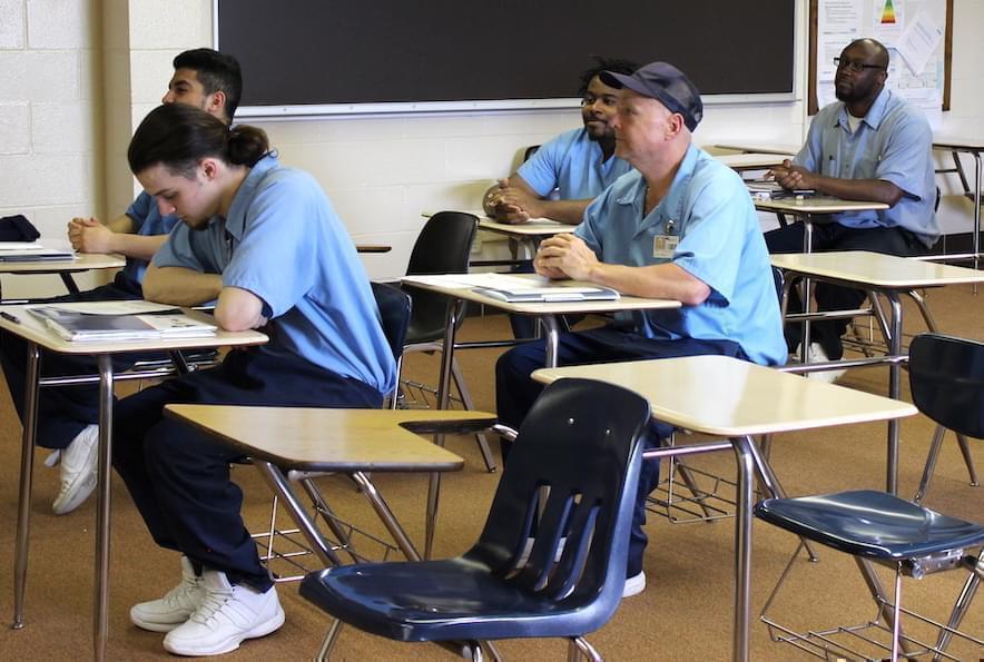 Incarcerated men sit at classroom desks inside a classroom at an Illinois prison