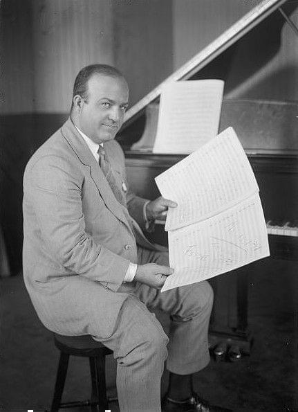 Ferde Grofe posing by piano with sheet music.