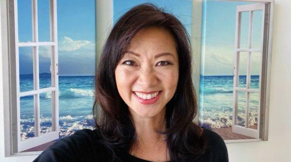 Lisa Kumagai in front of a window with the ocean shown in the background.