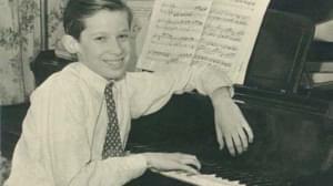 Young boy sits at piano smiling at the camera