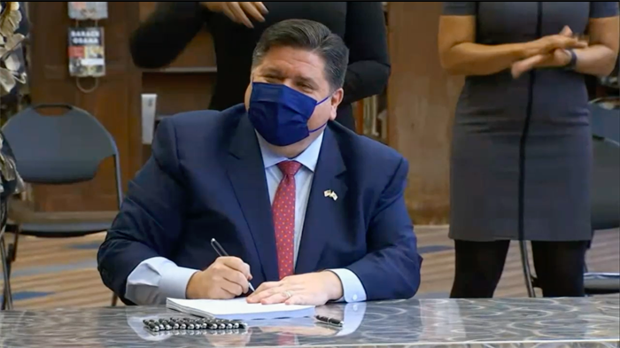 Gov. JB Pritzker gives House Bill 2170 his final signature, flanked by Lt. Gov. Juliana Stratton and members of the Illinois Legislative Black Caucus, during an event at Proviso East High School on Monday.