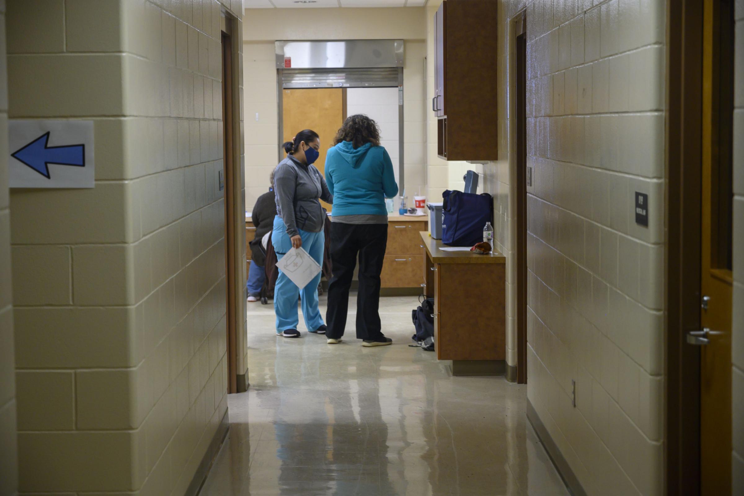 Tama County Public Health Executive Director Shannon Zoffka (right) speaks to a volunteer at the county's COVID-19 vaccination clinic at the former Girls State Training School in Toledo, Iowa.