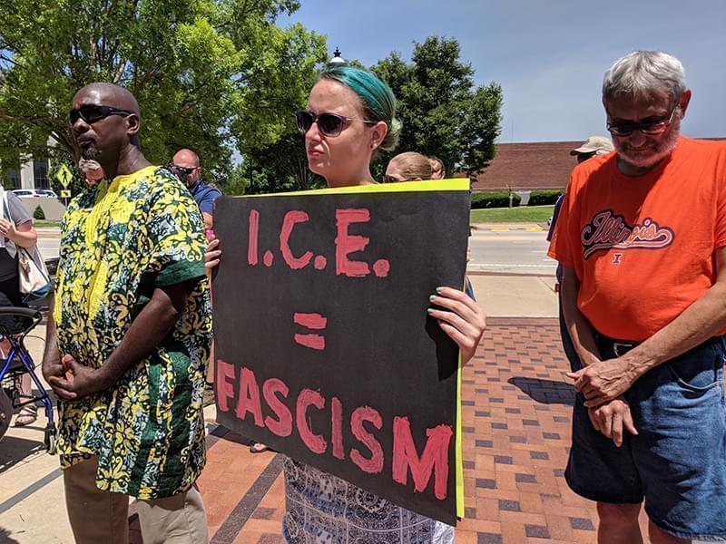A woman holding a sign saying ICE equals fascism standing next to a male protester
