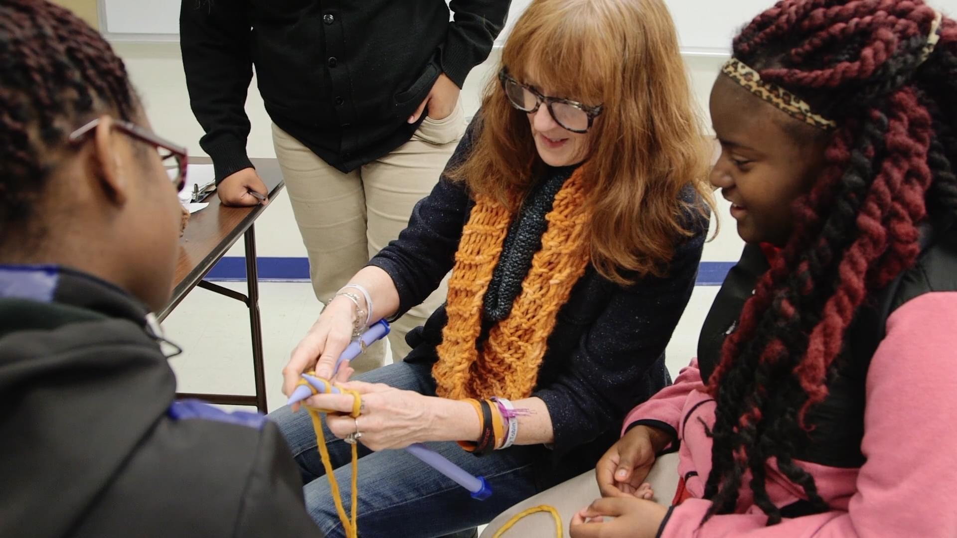 Woman teaches two young girls how to knit