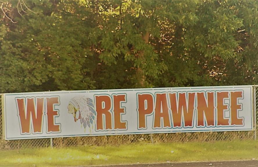 picture of a sign on a fence that says we are pawnee but the a is replaced with Native American imagery