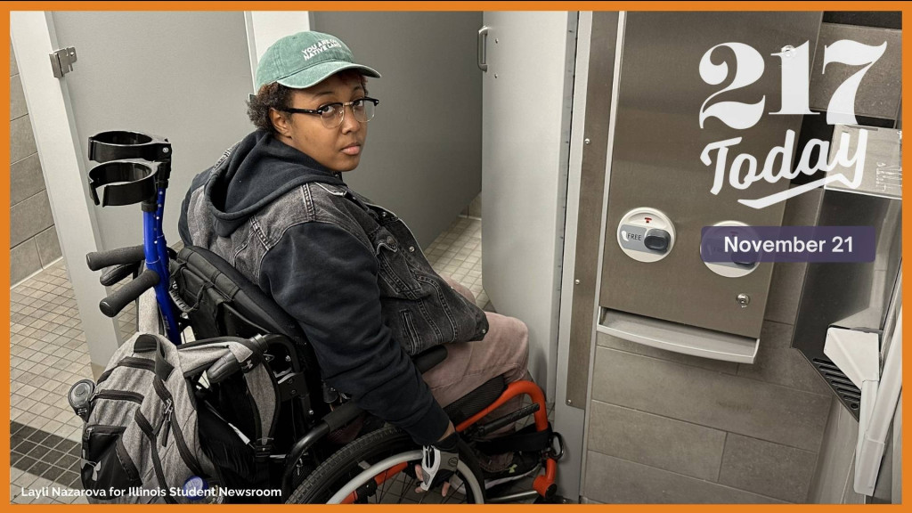 Alyx Bibbs, a wheelchair user at the University of Illinois Urbana-Champaign, demonstrates how their wheelchair does not fit in the stall in the women’s bathroom in Room 135 in the Henry Administration Building. The “wheelchair-accessible” signage was removed in mid-November, after Bibbs decided to drop their class. 