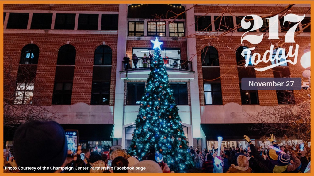 People surround a lit up tree in front of a building.