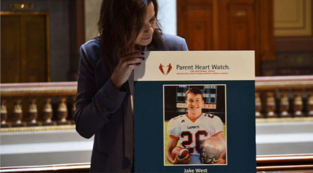 Julie West holds a poster of her son, Jake, inside the Indiana Statehouse on Wednesday, March 22, 2023. Jake died from an undetected heart condition, and collapsed while playing football at his school.