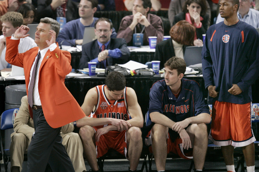 Former Illinois coach Bruce Weber in front of basketball players sitting on a bench. 